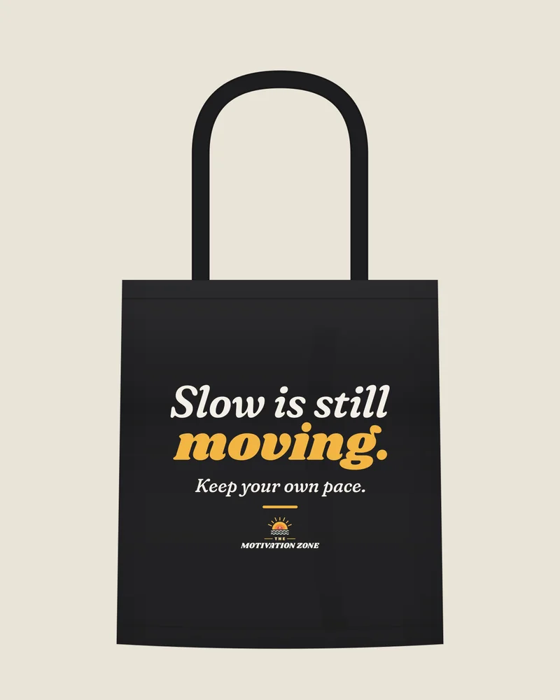 Black tote bag with the print “Slow is still moving.”, front view (illustration)